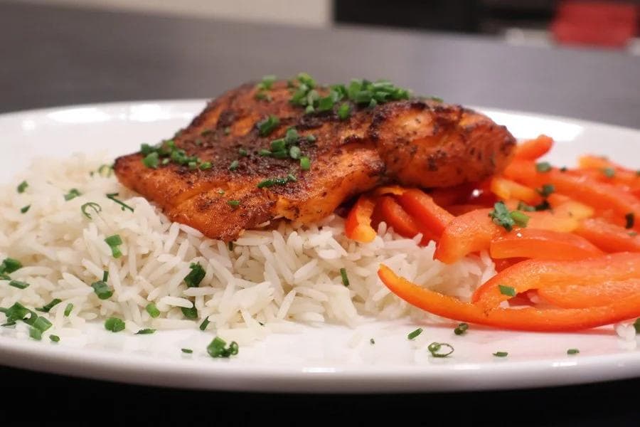 Air fryer salmon with crispy seasoned crust on white rice with sautéed red peppers and green onion garnish.