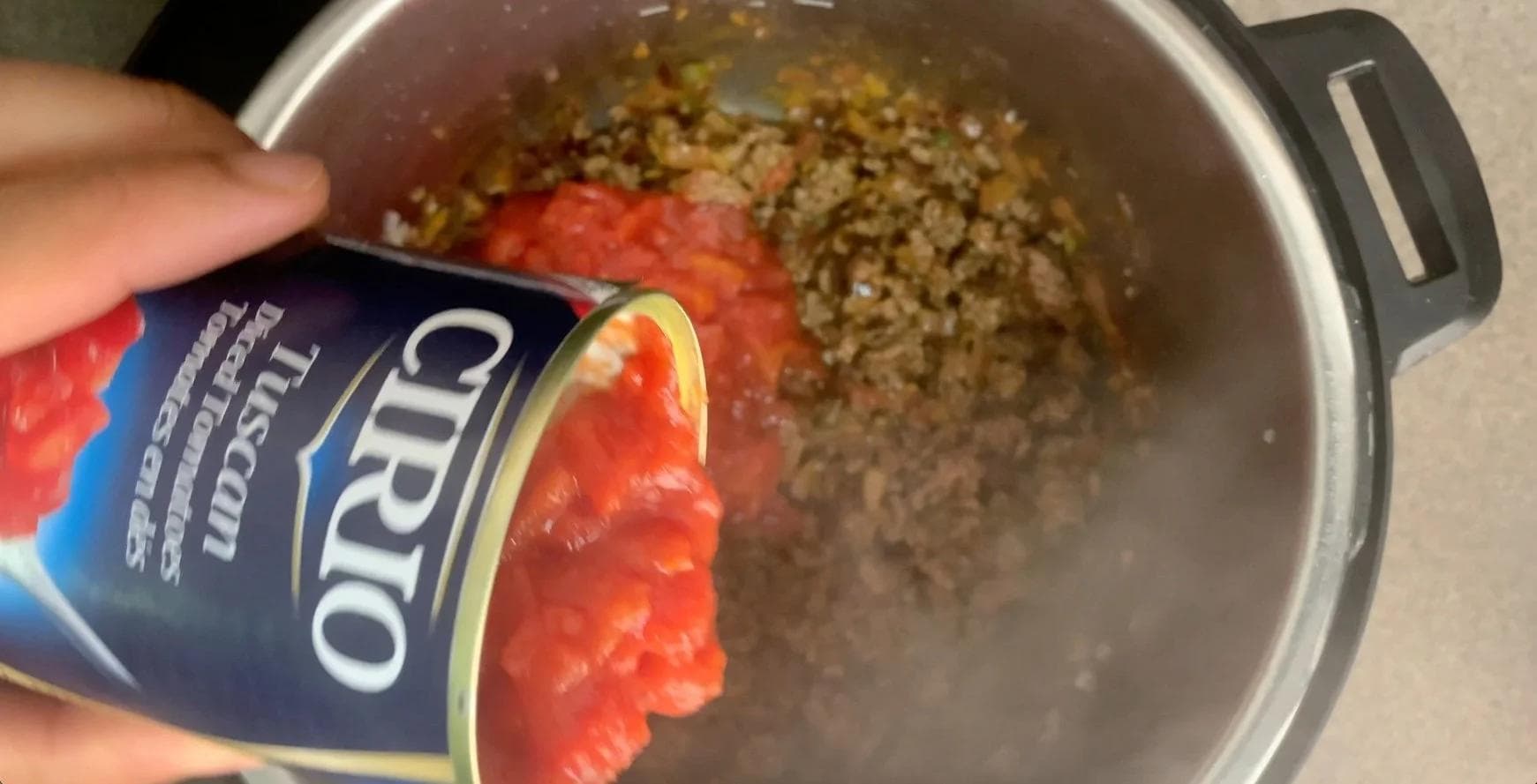 Pouring canned diced tomatoes into Instant Pot with cooked ground beef and spices for chili.