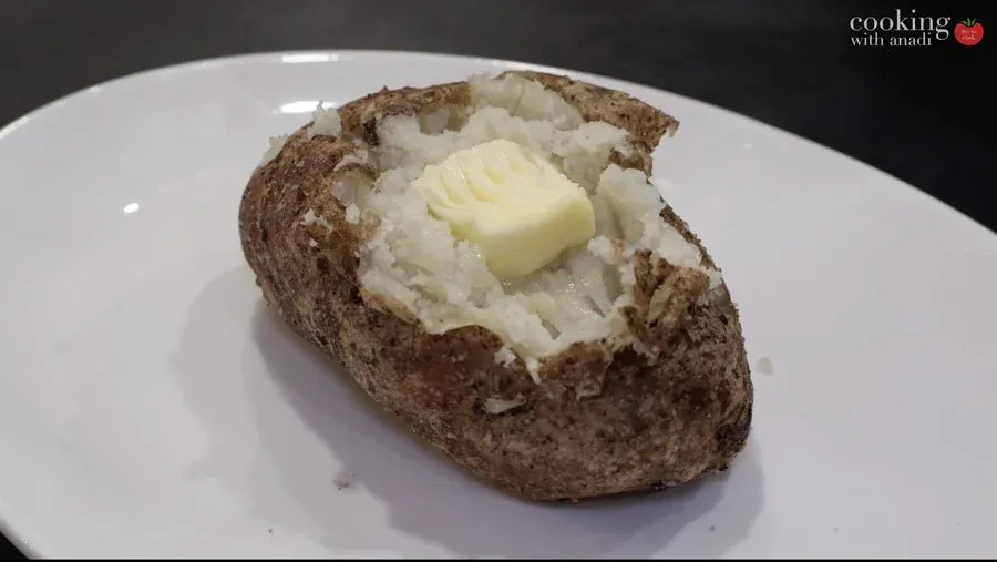 Baked potato split open with fluffy white flesh and a pat of melting butter on top, served on a white plate.