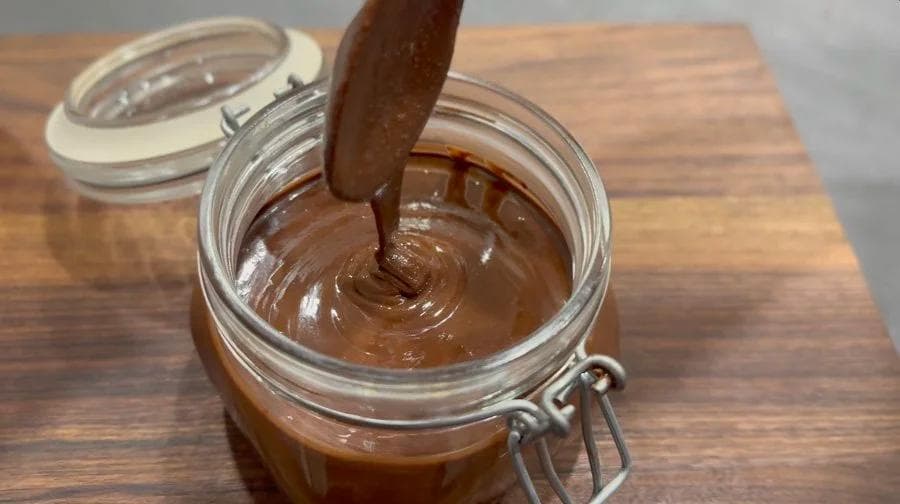 Chocolate hazelnut spread being stirred in a glass jar with a wooden spoon on a wooden surface