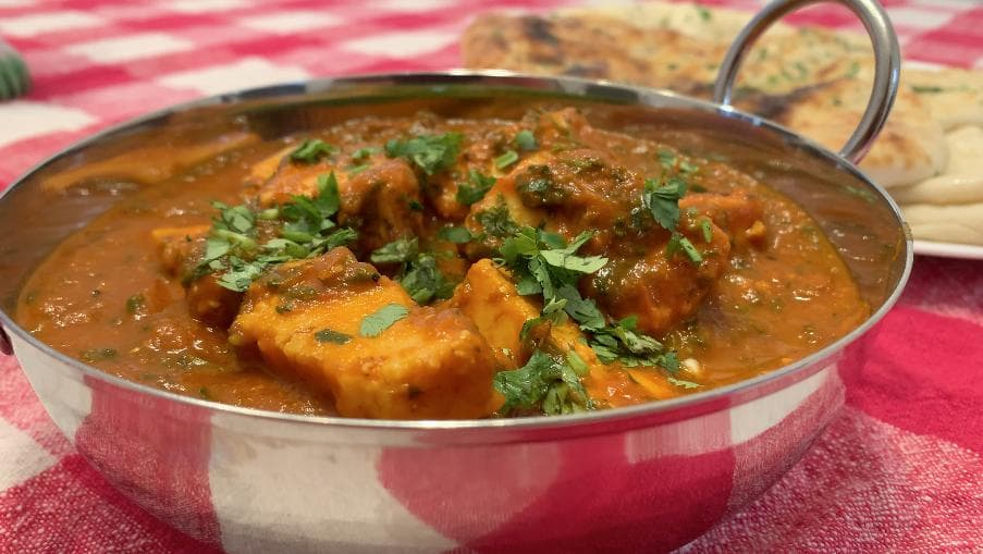 Adraki Dhaniya Paneer served in a traditional metal bowl, garnished with fresh cilantro on a pink checkered cloth.