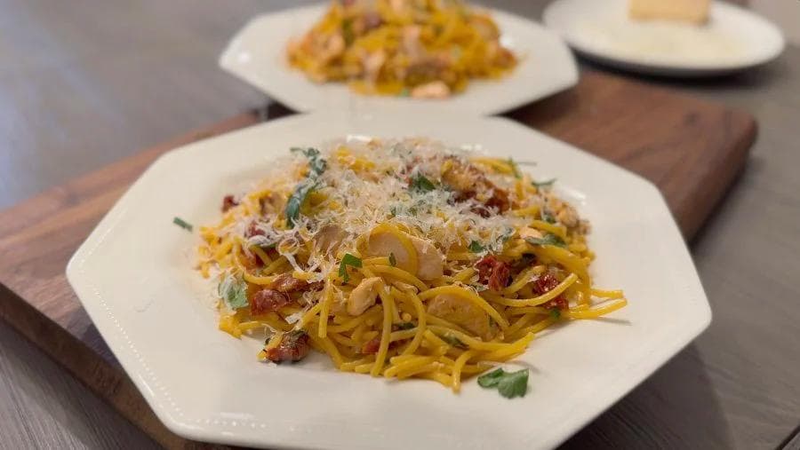 Plated lemon salmon spaghetti with grated cheese and fresh herbs on white dishes.