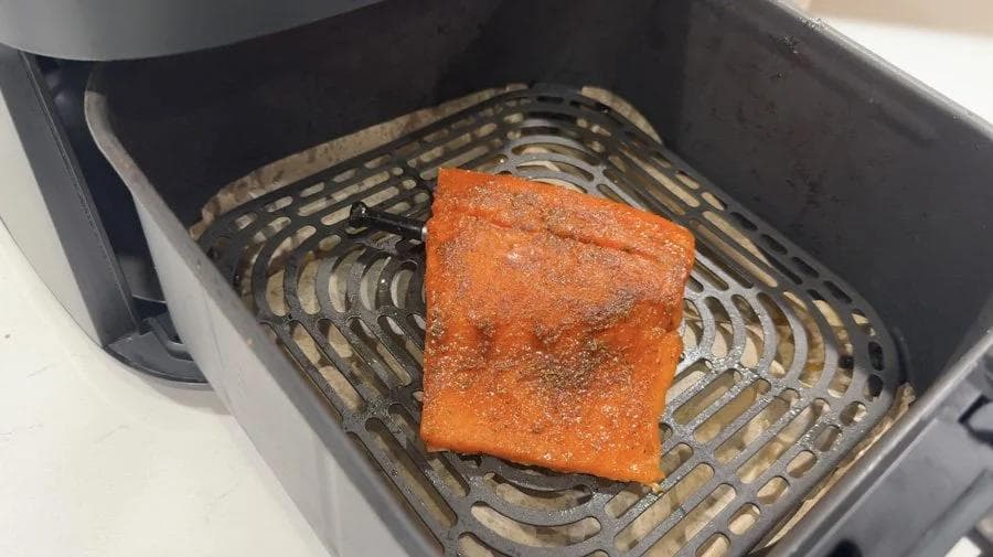 Seasoned salmon fillet skin-side down in air fryer basket with spice rub applied.