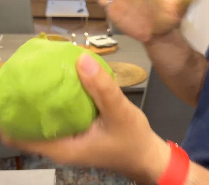 Hands kneading bright green spinach dough into a smooth ball on a kitchen counter.