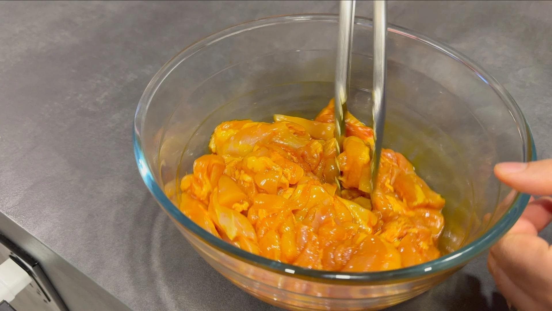 Saffron-infused marinade with chicken pieces in a glass bowl being stirred with a spoon.