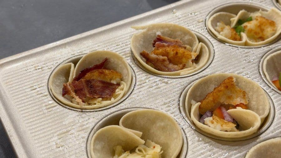 Baked egg cups in a muffin tin with various fillings including bacon, cheese, and vegetables visible in the cooked cups.