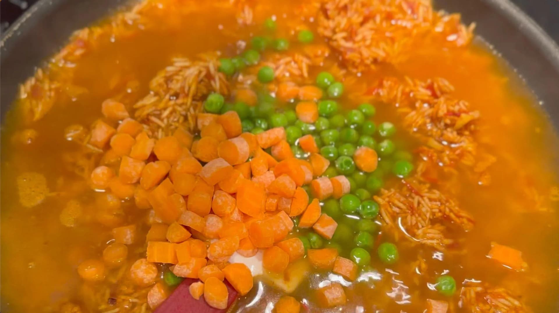 Mexican tomato rice simmering in a pot with carrots, peas, and chicken broth added.