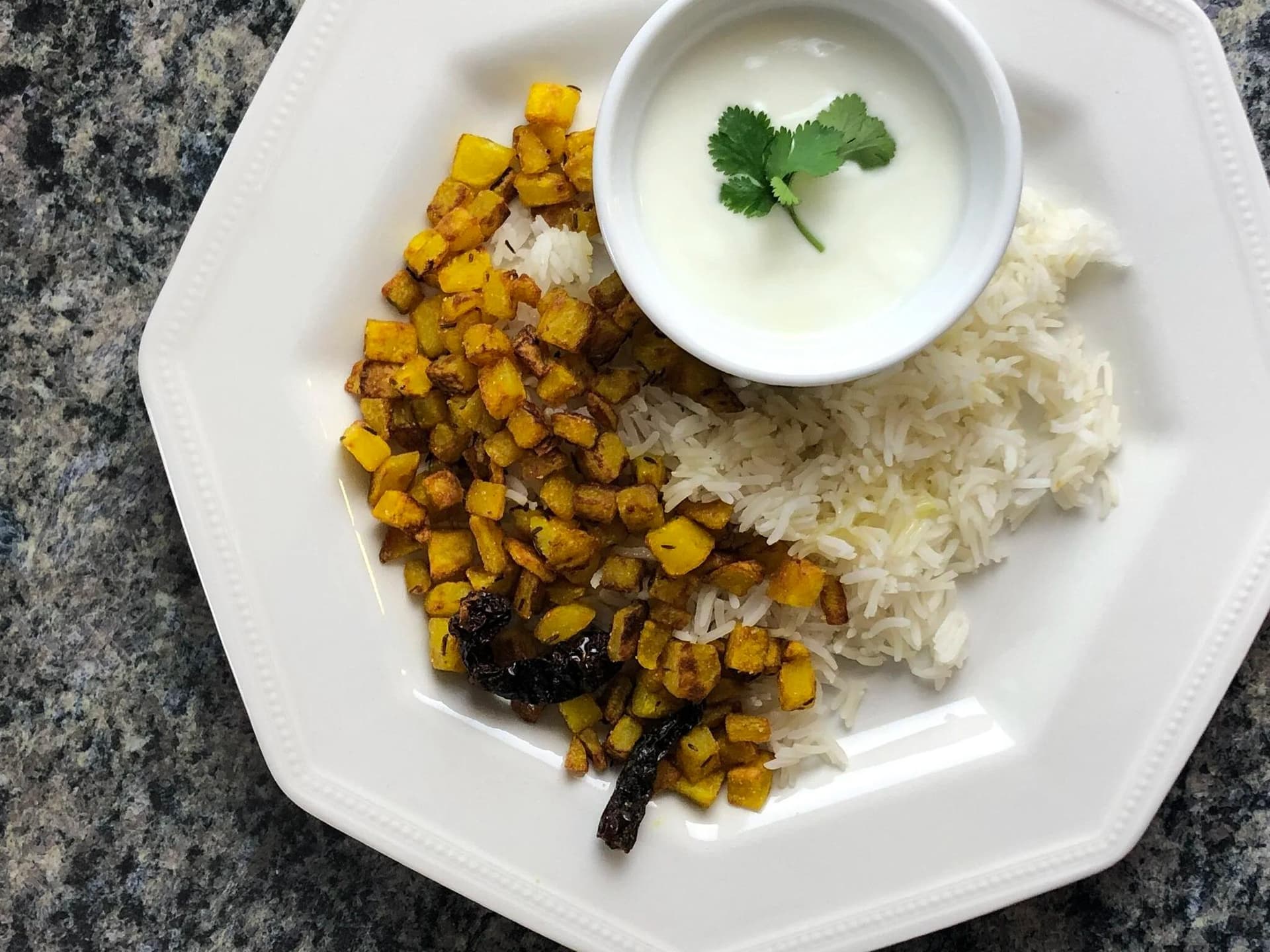 Crispy golden aloo bhujia served with white rice and yogurt raita garnished with cilantro on a white plate.
