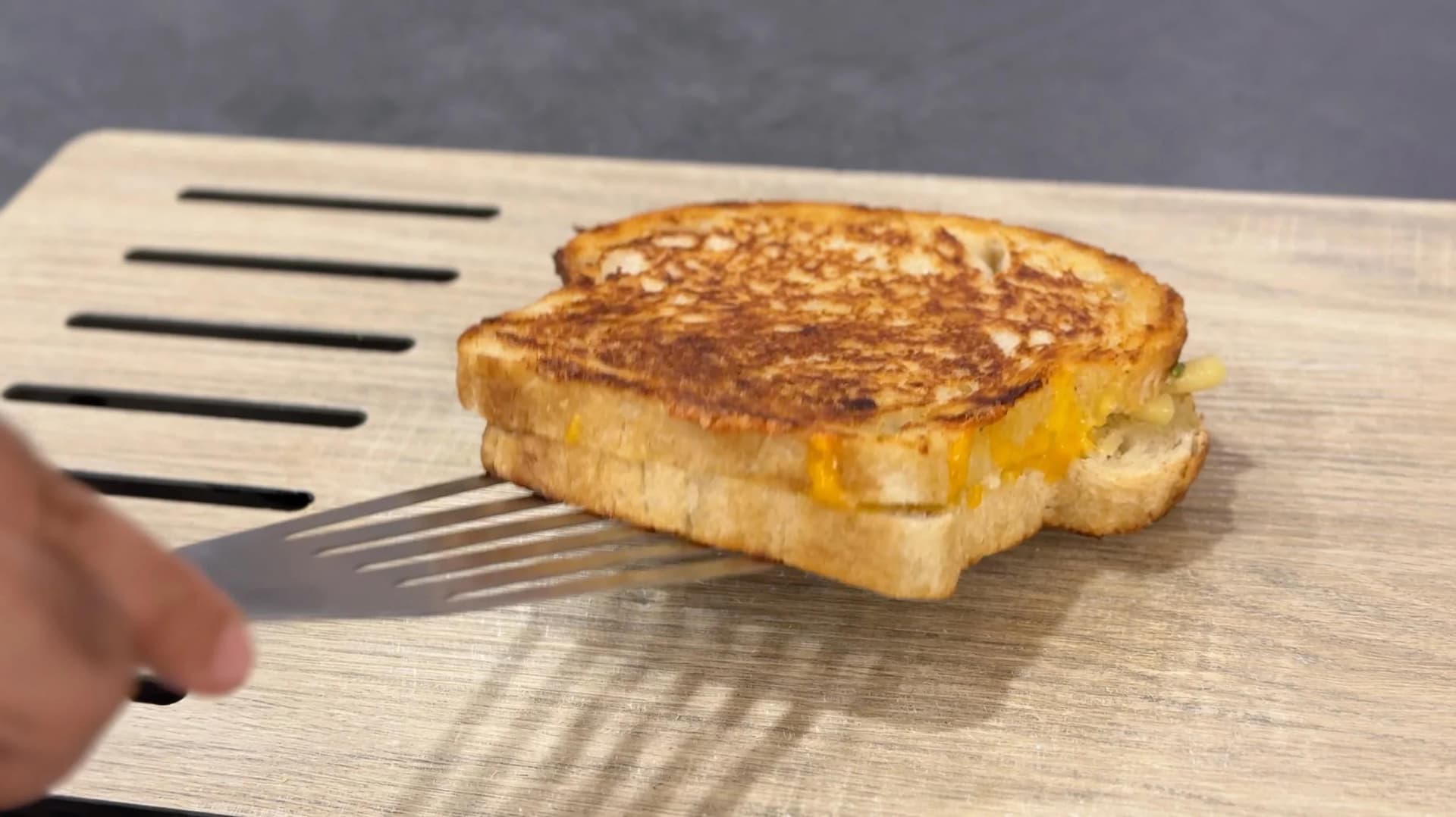 Golden-brown grilled cheese sandwich with melted cheese visible, being lifted with a spatula on a wooden surface.