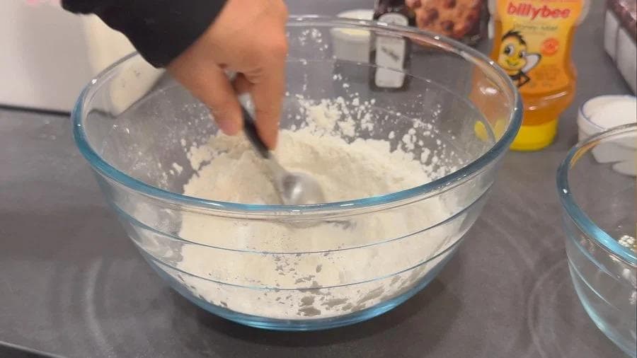 Hand whisking dry ingredients including flour and baking powder in a glass mixing bowl.