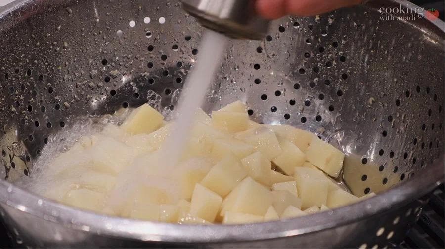 Cubed potatoes being drained in a colander after rinsing.