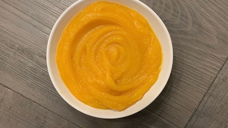 Homemade pumpkin puree in a white bowl with a smooth, creamy texture and golden-orange color.