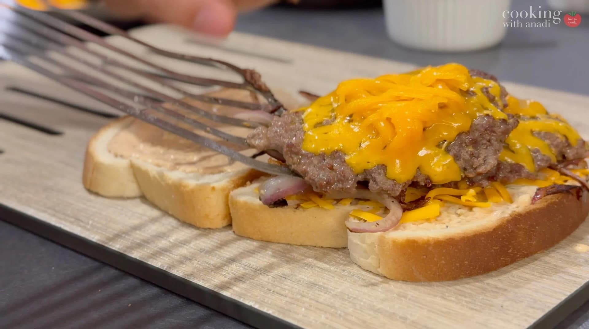 Smash burger patty melt on toasted bread with melted cheddar cheese, bacon strips, and onions on a wooden board.