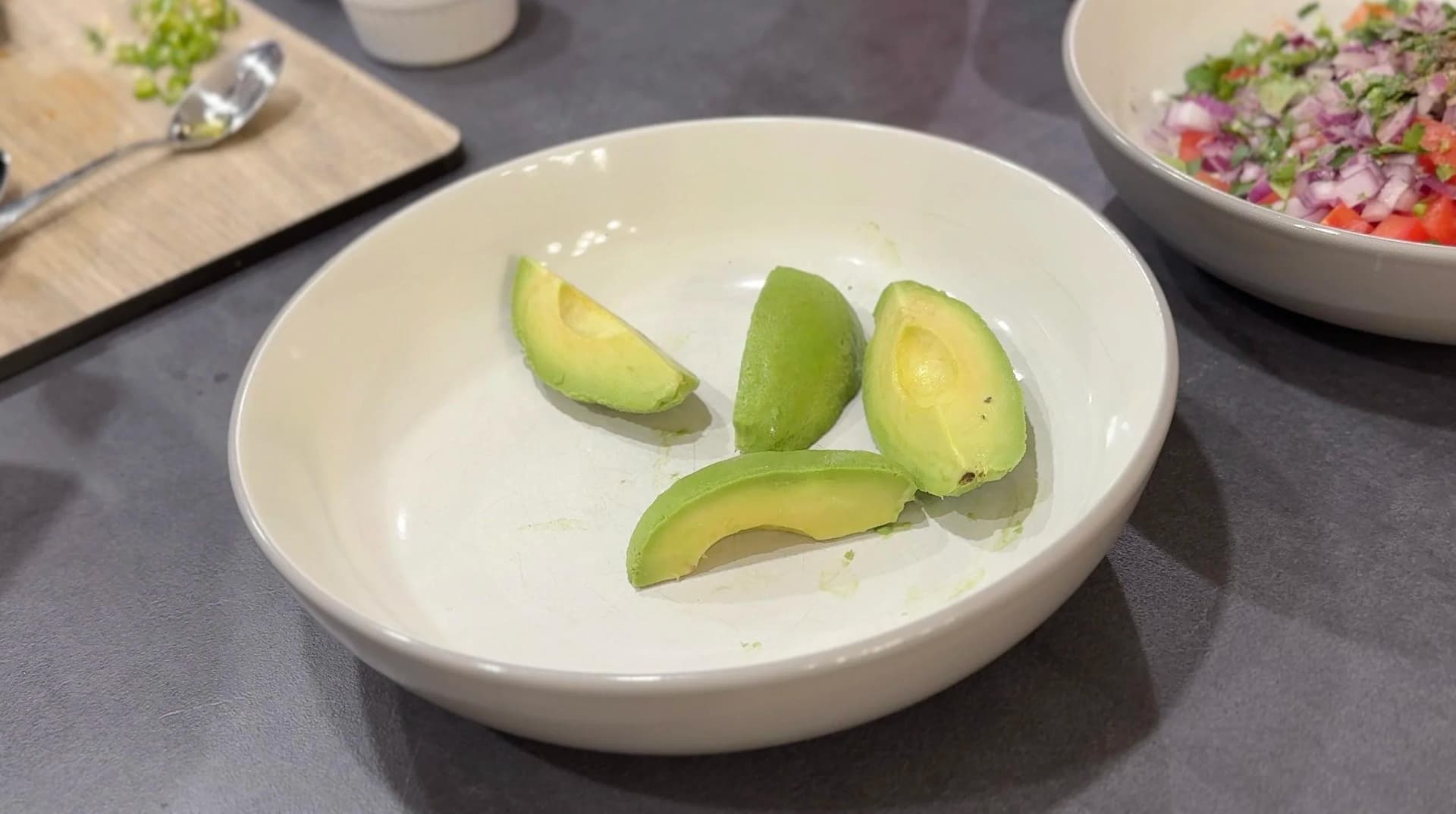 Sliced avocado halves arranged in a white bowl before mixing into guacamole.