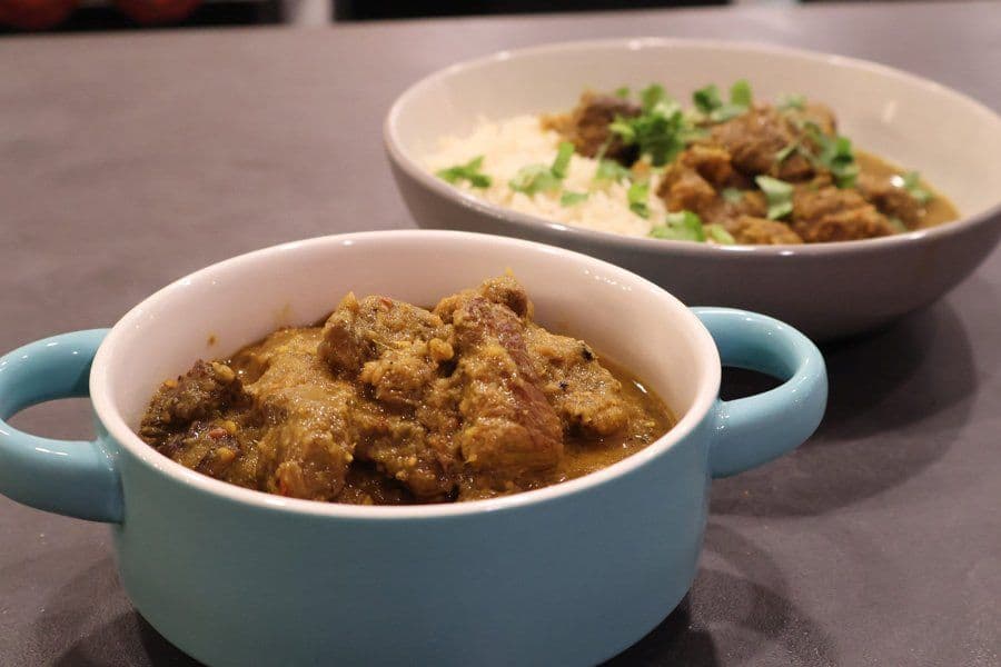 Stovetop Balinese beef rendang served in a light blue bowl with creamy base and garnished with green onions.