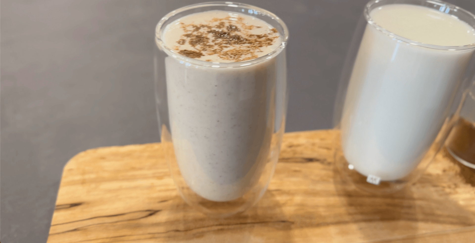 Two glasses of creamy white Mattha yogurt drink topped with ground spices on a wooden board.
