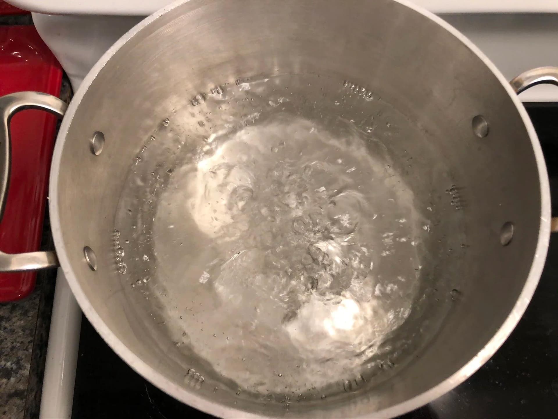 Boiling water with pasta in a stainless steel pot on the stovetop.