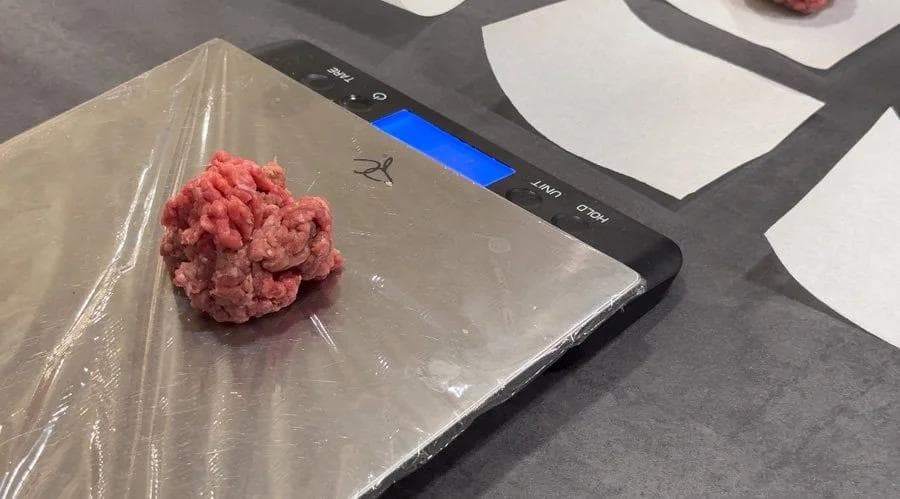Raw ground beef portion rolled into a ball and placed on parchment paper on a kitchen scale.
