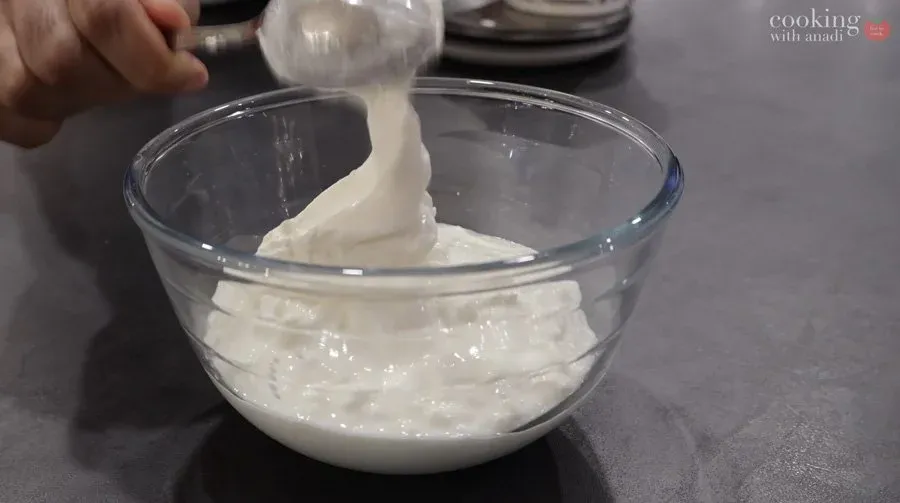 Pouring sour cream into a glass bowl of cottage cheese mixture for strukli filling