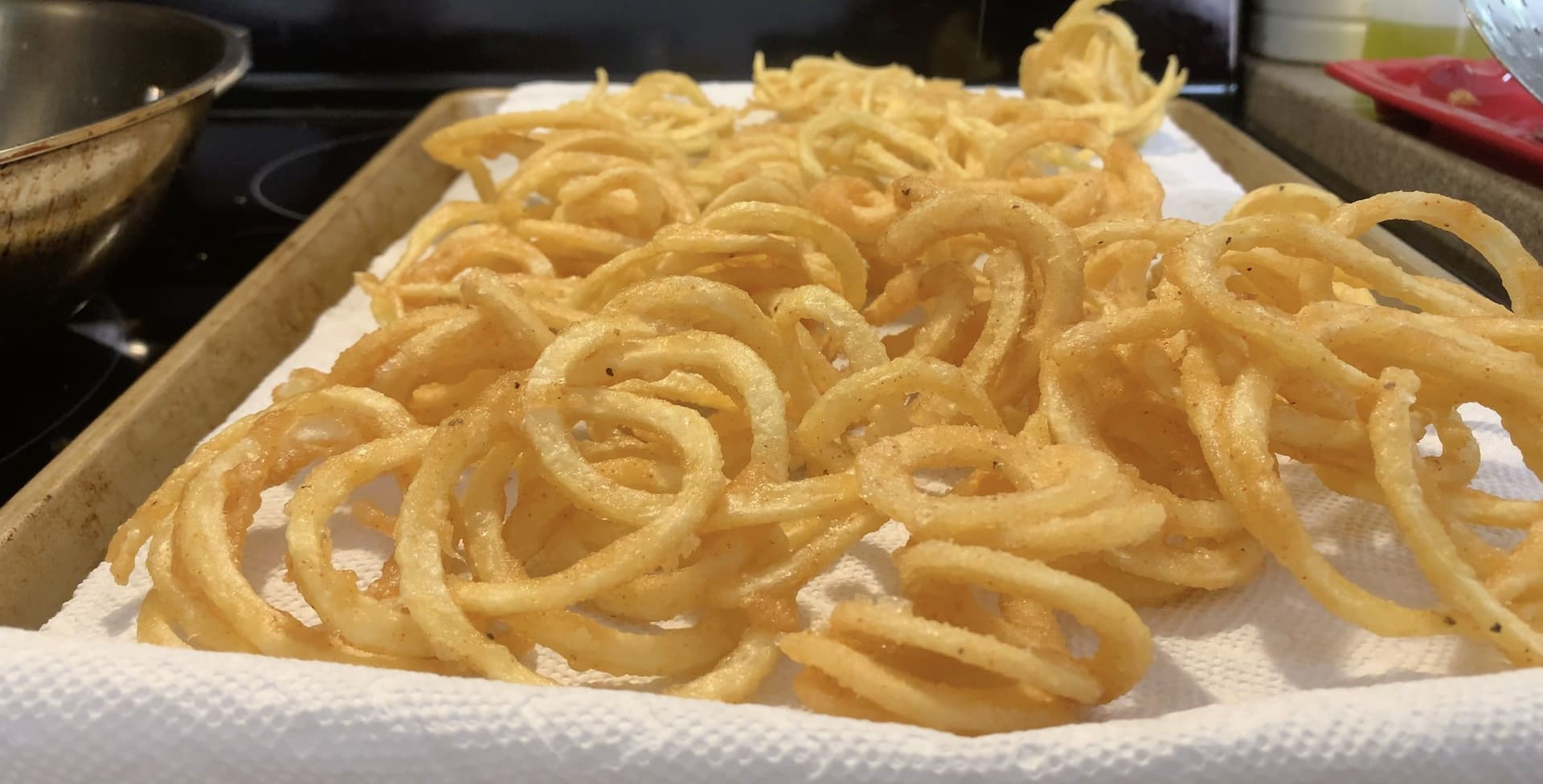 Golden crispy curly fries cooling on white paper towels in a cardboard-lined tray.