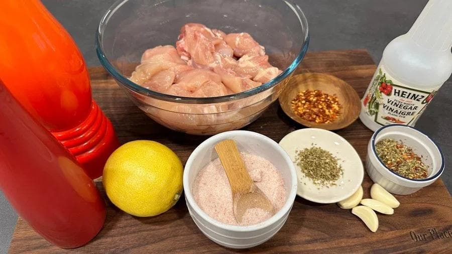 Souvlaki marinade ingredients including raw chicken cubes, lemon, garlic, oregano, vinegar, and spices arranged on a wooden board.