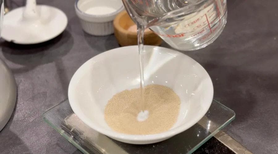 Water being poured into a bowl of yeast mixture for Canadian Beavertails dough.