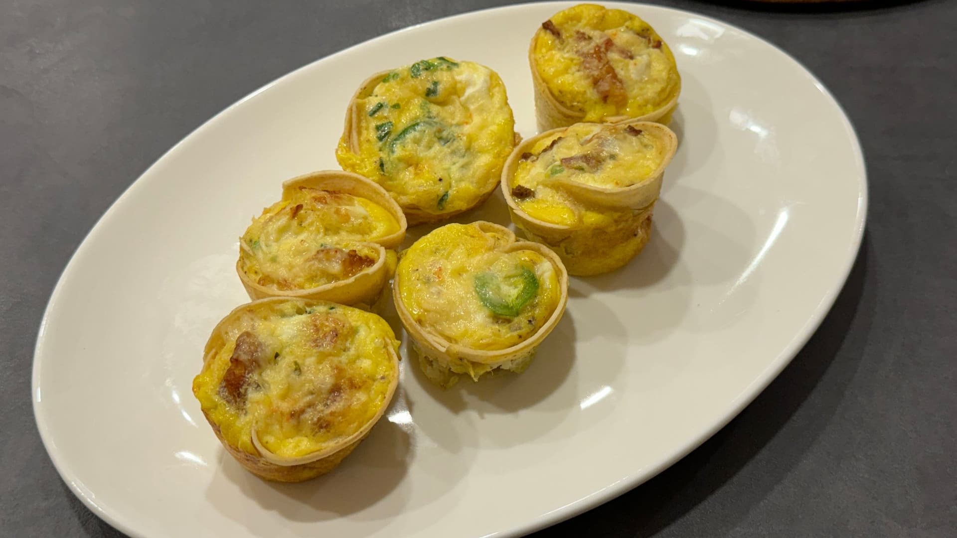 Six baked tortilla egg cups with eggs and herbs on a white plate.