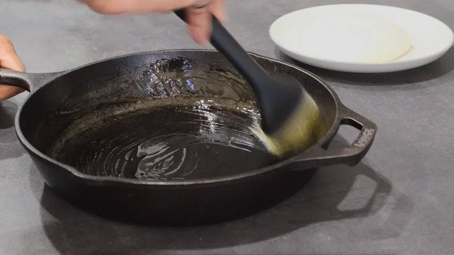 Oiling a cast iron skillet with a brush for pizza preparation.