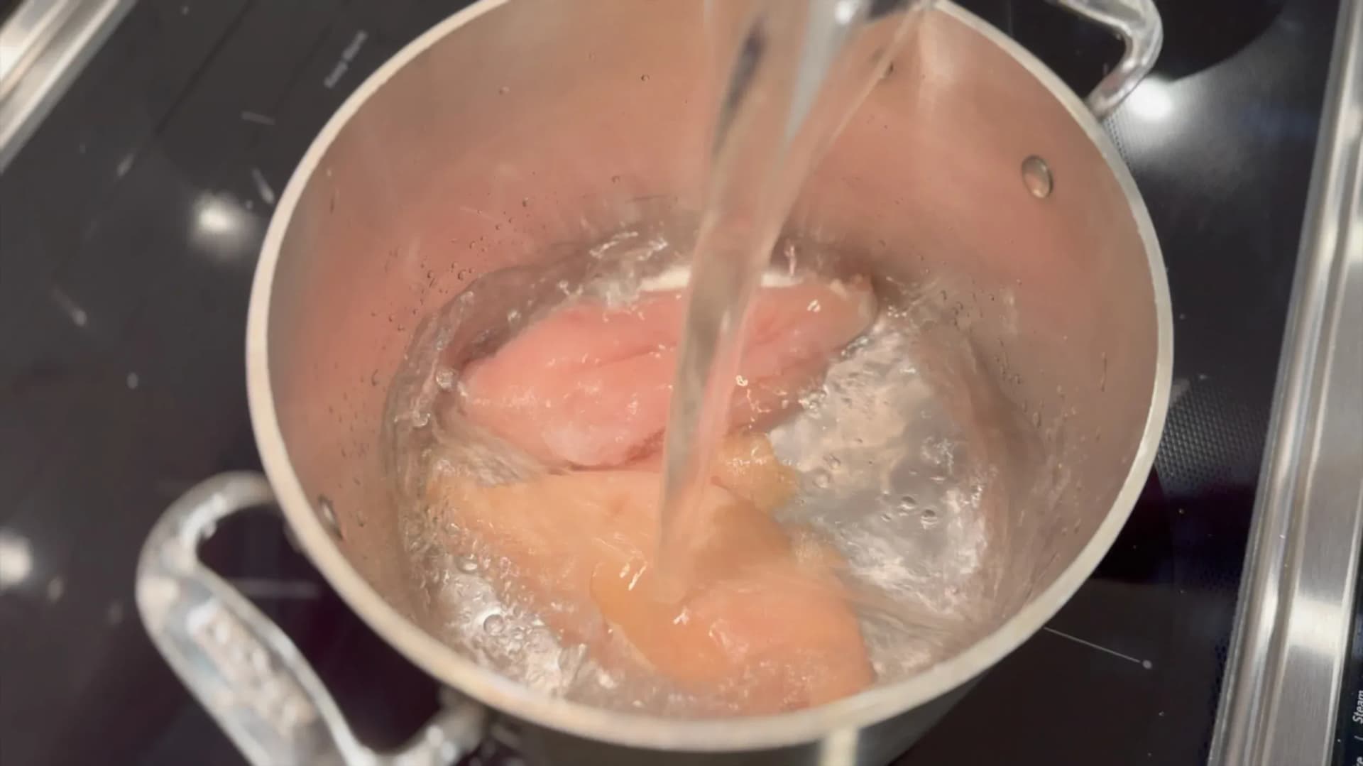 Chicken breasts simmering in gently boiling water in a pot on the stove.