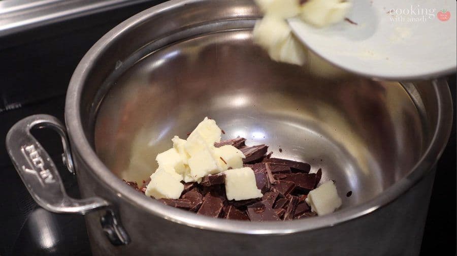 Chopped dark chocolate and butter chunks in a stainless steel bowl over simmering water for melting.