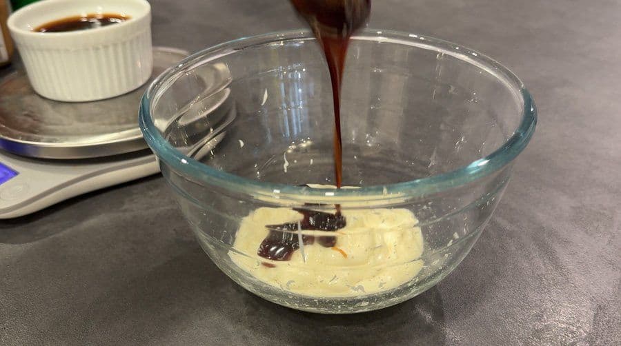 Dark sauce being poured into a glass bowl of creamy white mixture for Osaka spicy umami sauce.