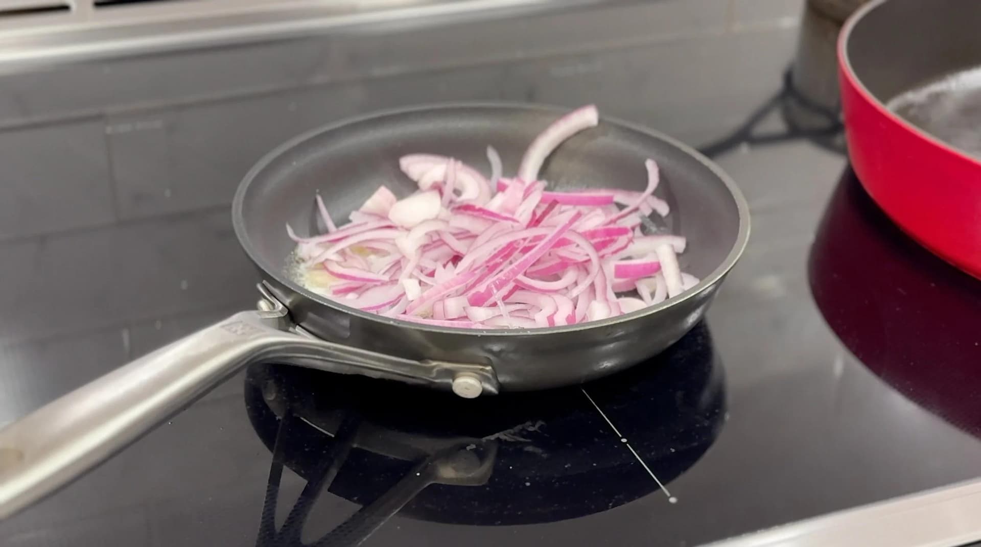 Sliced pink onions caramelizing in melted butter in a skillet on a stovetop.