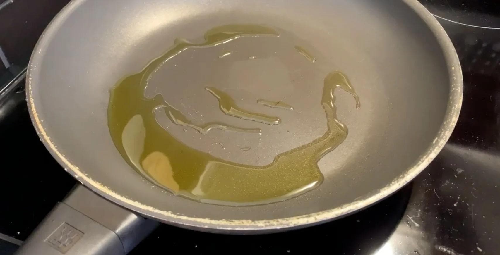 Salmon fillet cooking skin-side down in olive oil in a non-stick pan on stovetop.