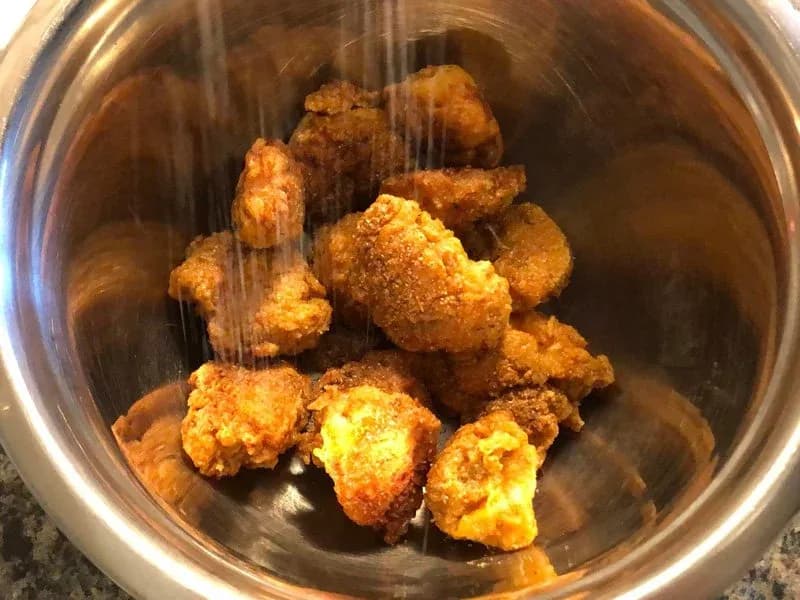 Crispy fried chicken and shrimp pieces in a stainless steel bowl being patted dry with paper towels.