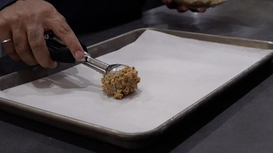 Using an ice cream scooper to portion cookie dough onto parchment-lined baking tray.