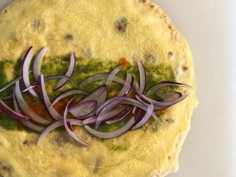 Purple onion slices layered on a green chutney-spread egg roll with tomato visible underneath.