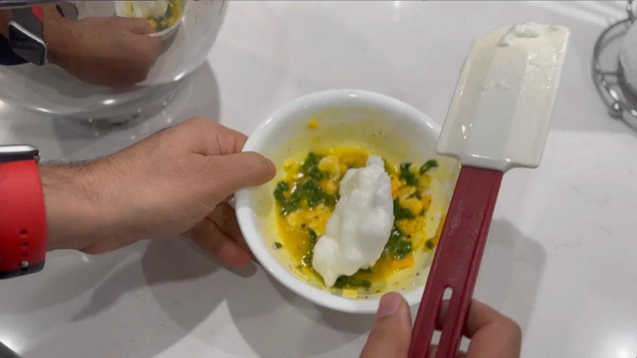 Hands holding a ramekin with a fluffy cheese soufflé topped with melted cheese and fresh herbs.