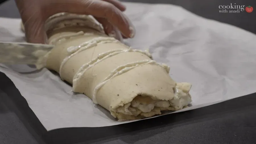 Rolled gluten-free strukli log with cheese filling being lifted on parchment paper, cut into segments.