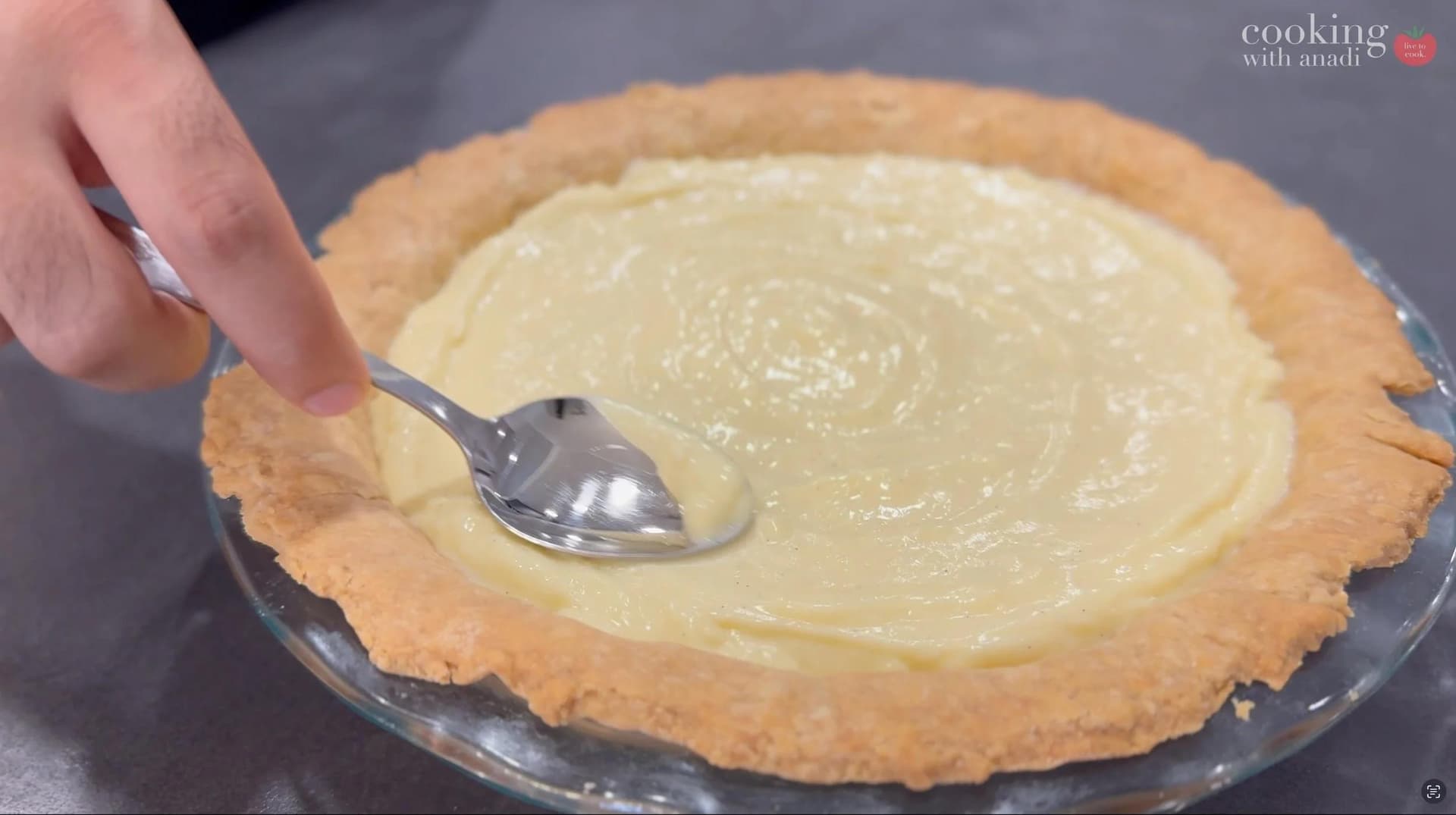 Smoothing creamy banana cream pie filling in a golden pie crust with a spoon.