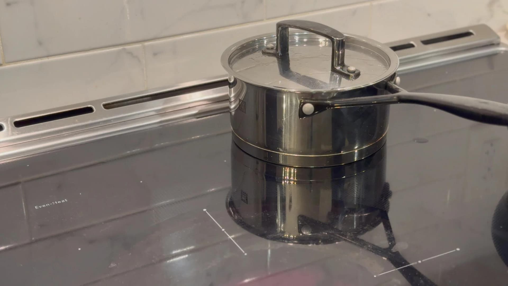 Stainless steel saucepan with glass lid on induction cooktop, filled with couscous and water mixture.