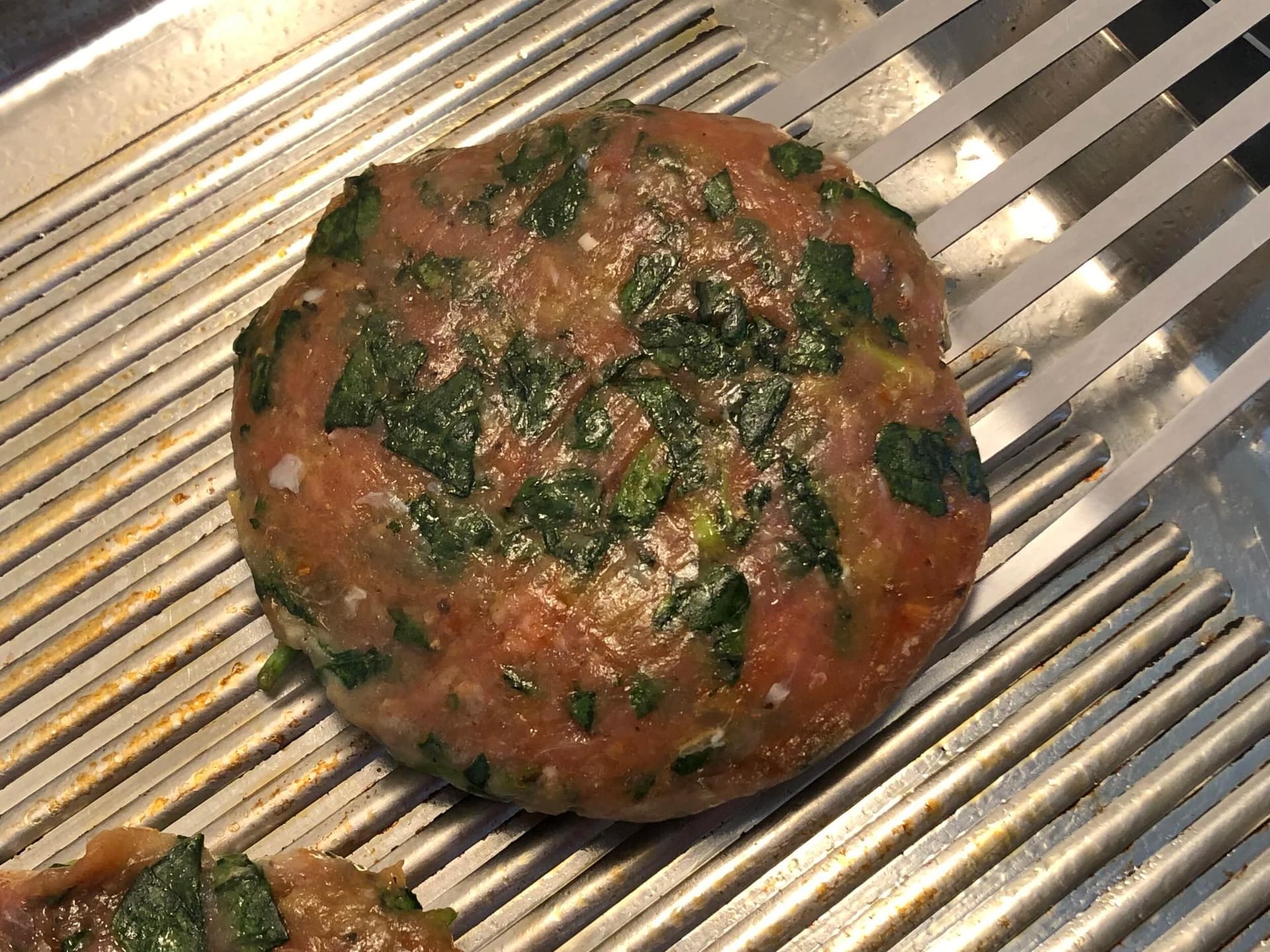 Spinach turkey burger patty cooking on grill pan, topped with melted cheese and fresh spinach garnish.