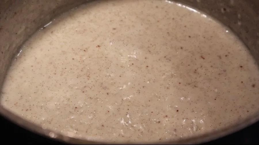 Creamy rice pudding simmering in a pot with visible vanilla bean specks and nutmeg throughout.