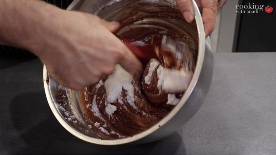 Folding whipped egg whites into chocolate mousse batter with a spatula in a white bowl.