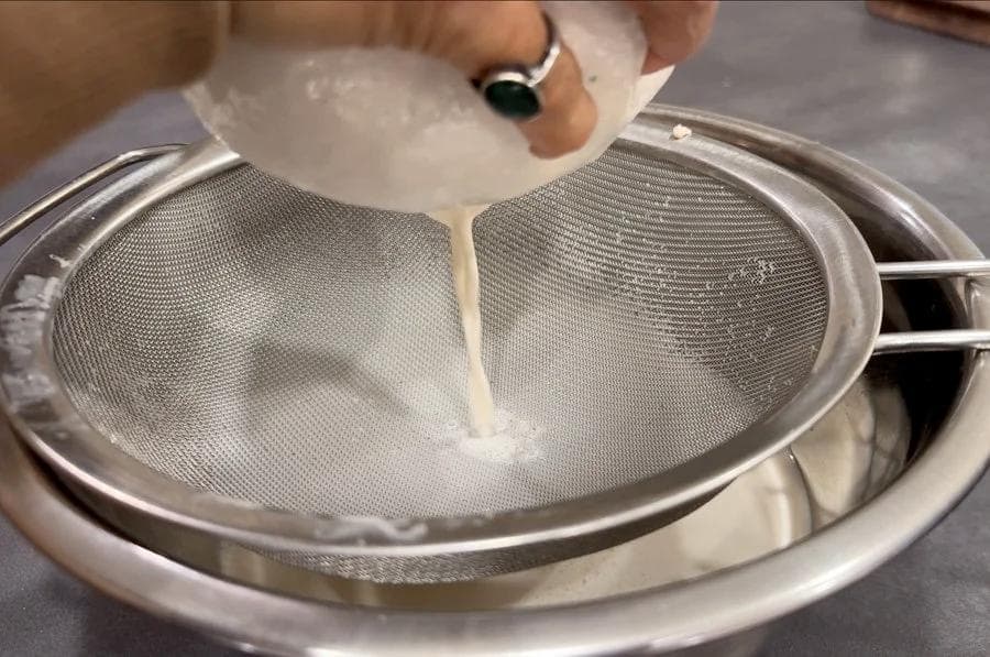 Straining almond milk through cheesecloth and sieve into a bowl.