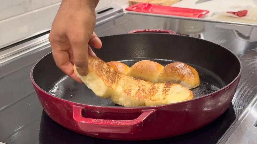 Hand placing parchment-lined turkey burger patties into a red skillet on the stovetop to cook.
