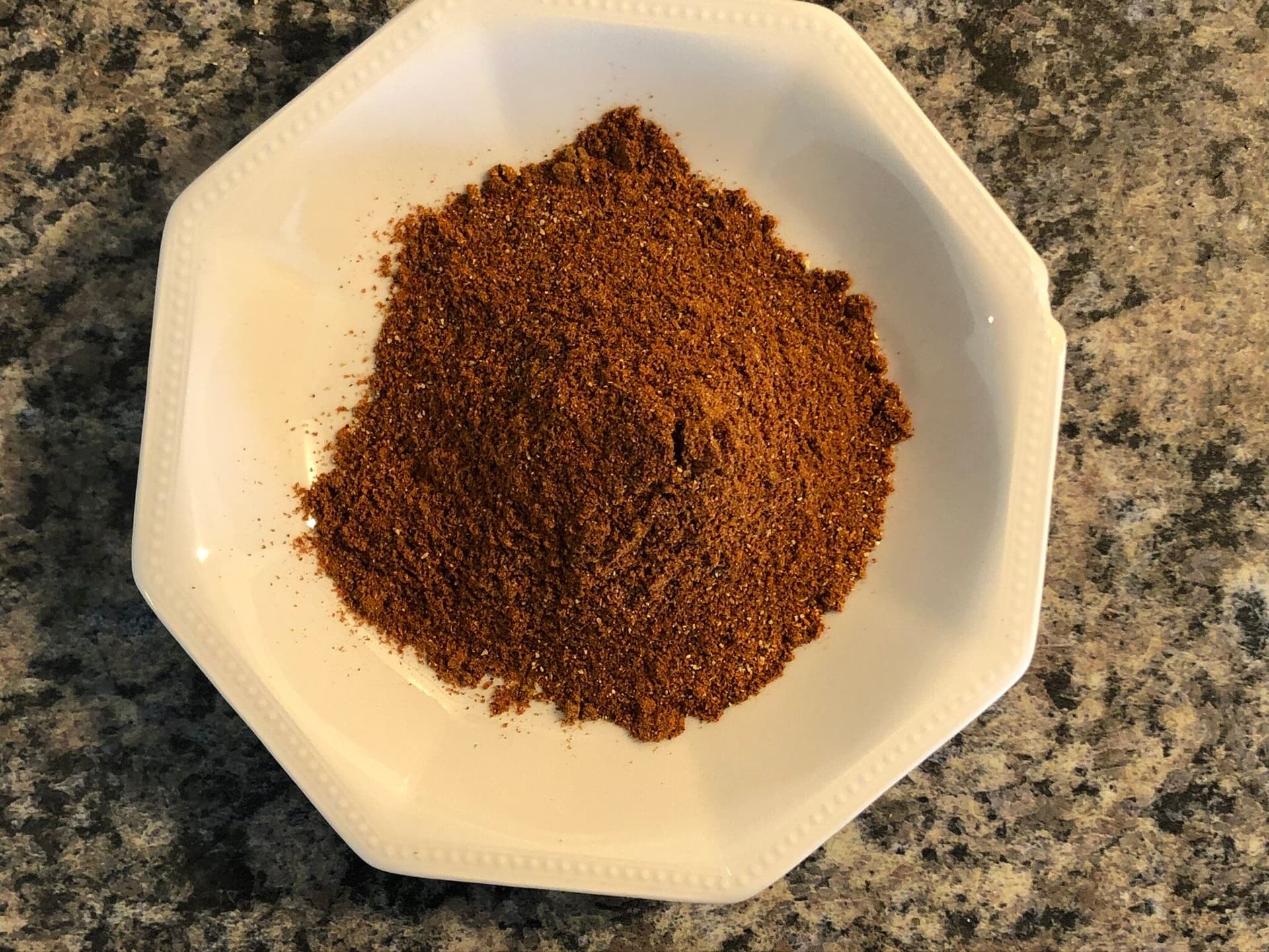 Homemade taco seasoning spice blend in white bowl on granite countertop.