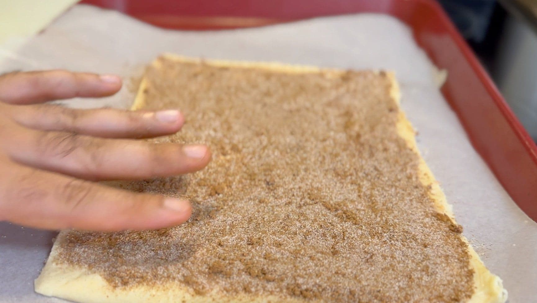 Hand sprinkling cinnamon sugar mixture over buttered crescent roll dough.