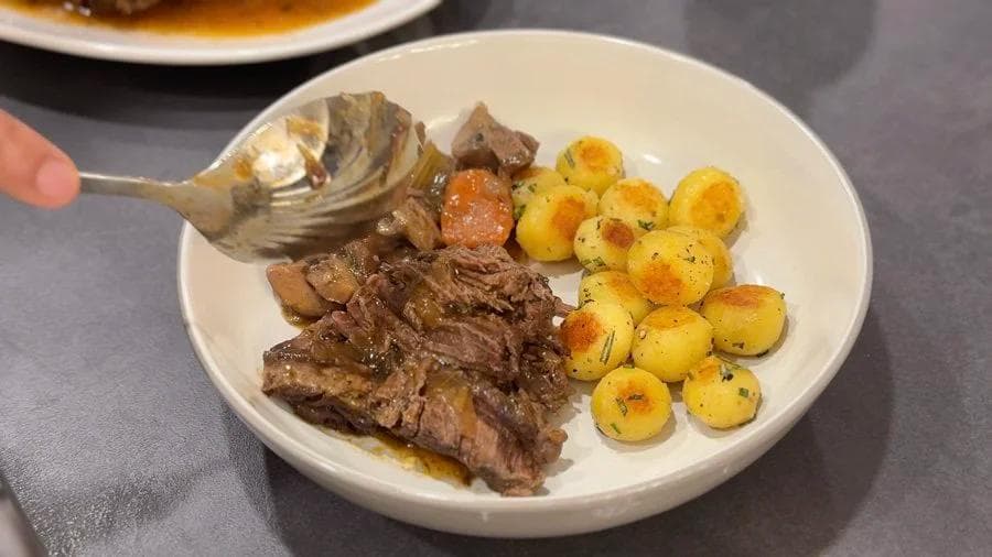 Sliced pot roast with roasted potatoes and carrots served on a white plate with gravy.