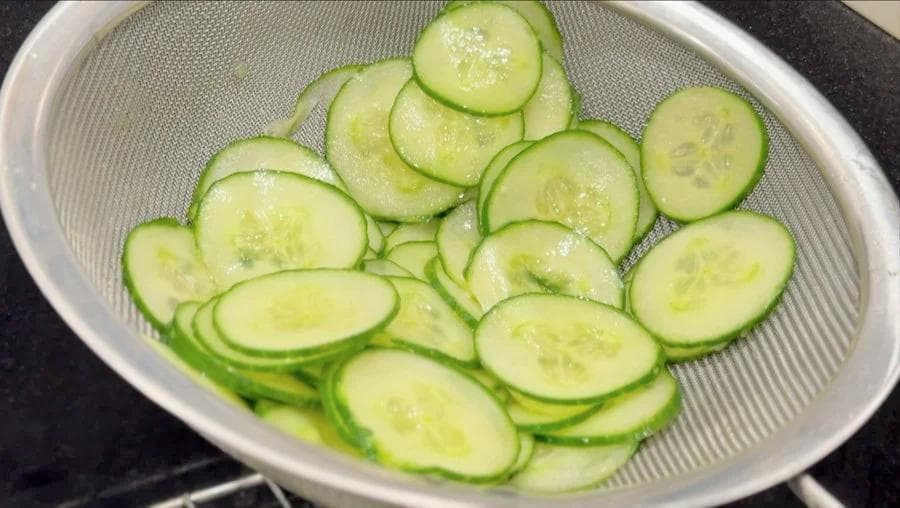 Thinly sliced cucumbers in a colander after being salted and drained.