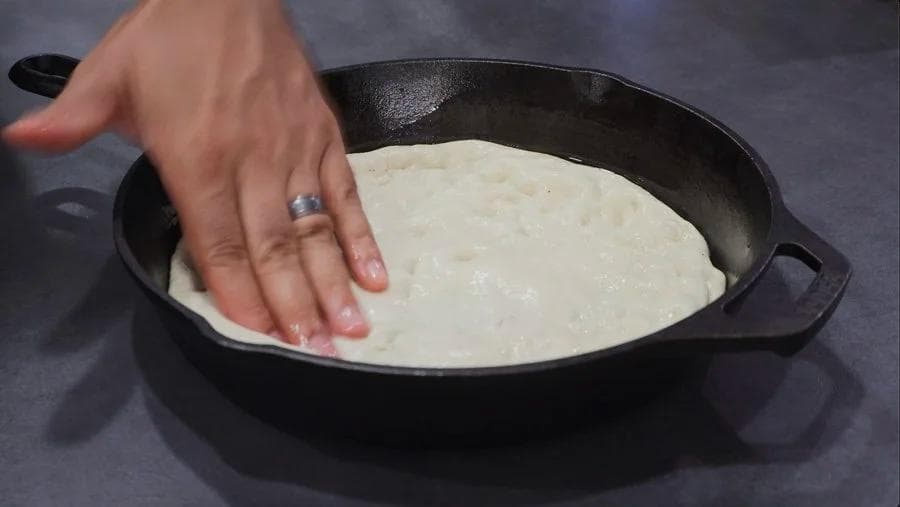 Hand stretching pizza dough to edges of cast iron skillet before adding toppings.